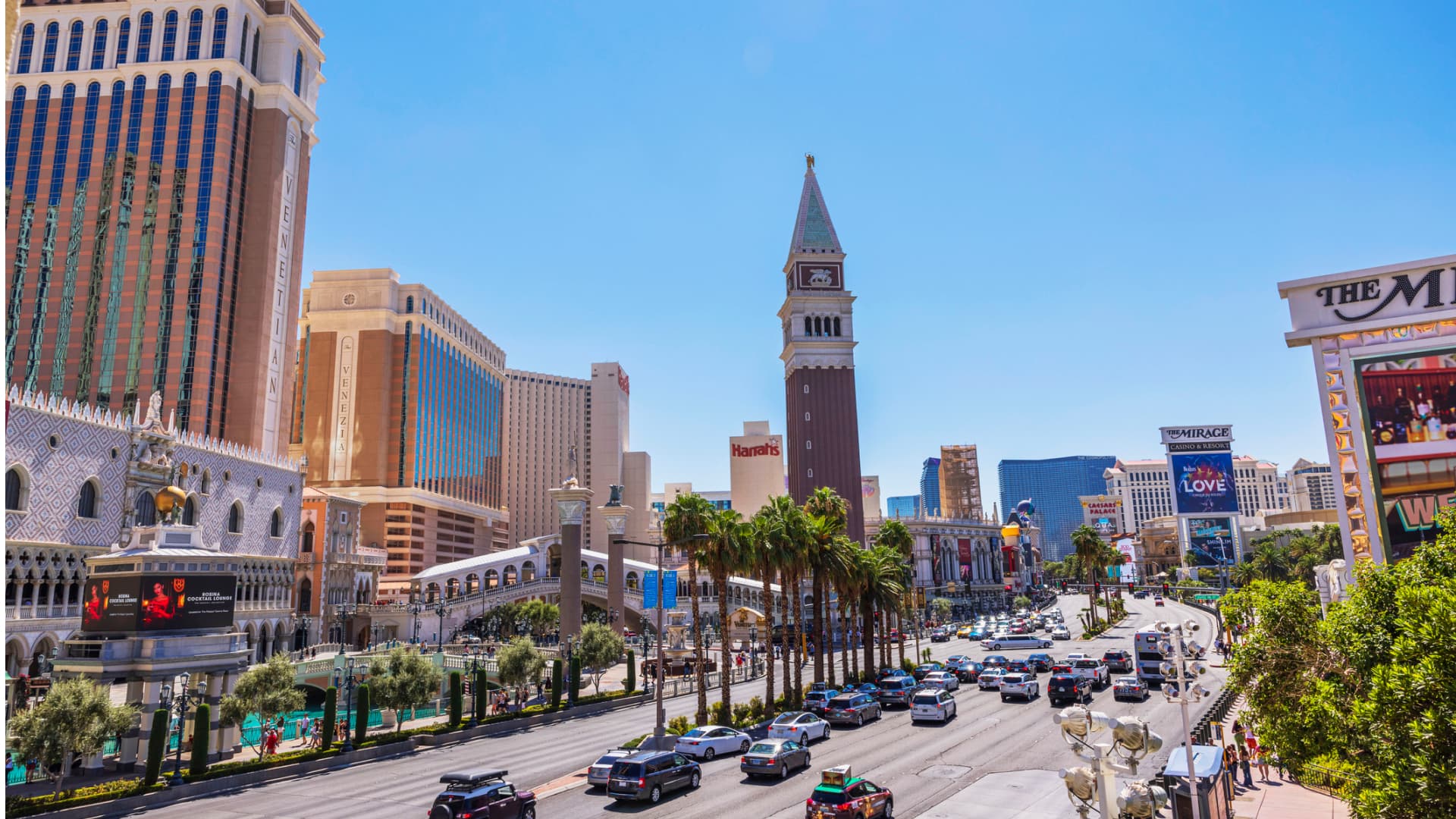 Street view of Las Vegas Strip featuring Venetian Hotel and Casino with busy traffic, palm trees, and vibrant cityscape under clear blue sky. stock photo